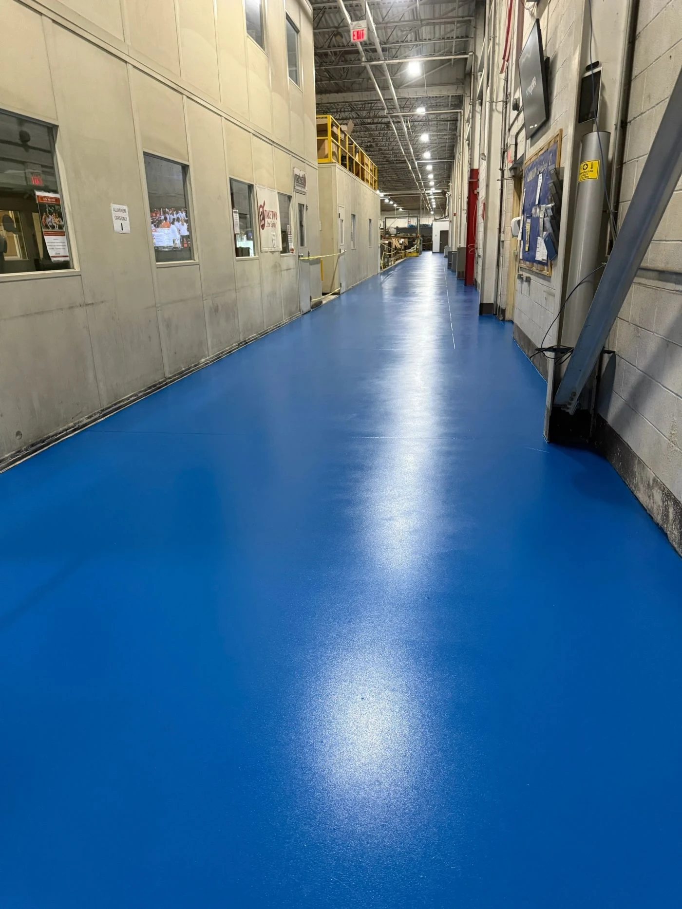 Blue industrial hallway flooring beside factory equipment and columns