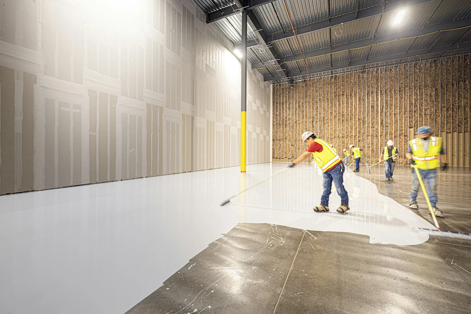 Workers applying a floor finish inside a large industrial building